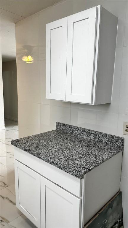 kitchen with marble finish floor, dark stone countertops, tile walls, and white cabinets