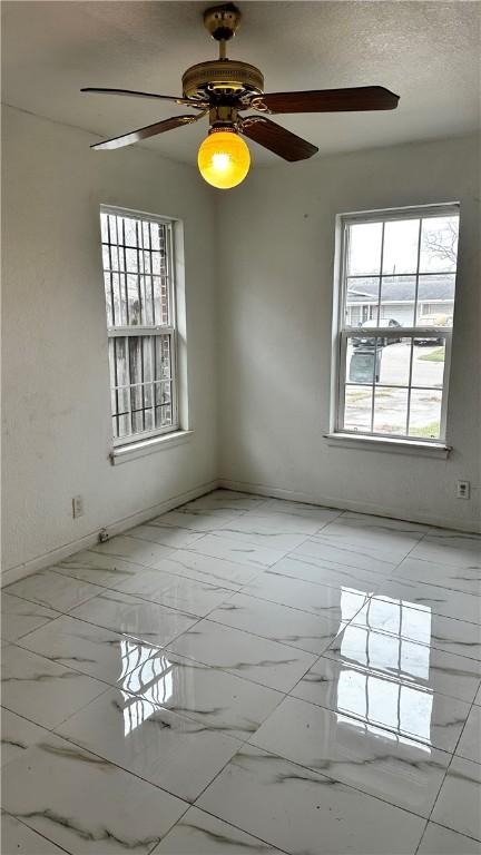 unfurnished room with a wealth of natural light, marble finish floor, a textured ceiling, and baseboards