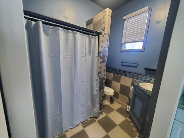 full bath featuring vanity, a wainscoted wall, tile patterned floors, toilet, and tile walls