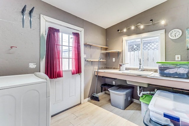 clothes washing area featuring a sink, baseboards, laundry area, and light wood finished floors