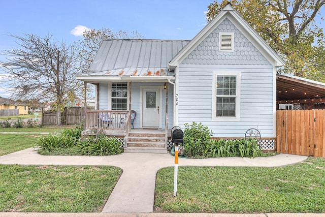 view of front of property with a standing seam roof, covered porch, a front lawn, and fence