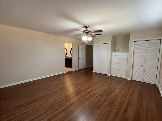 unfurnished bedroom featuring ceiling fan, dark hardwood / wood-style floors, ensuite bathroom, and two closets