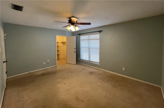 unfurnished bedroom with a walk in closet, ceiling fan, a closet, and light carpet