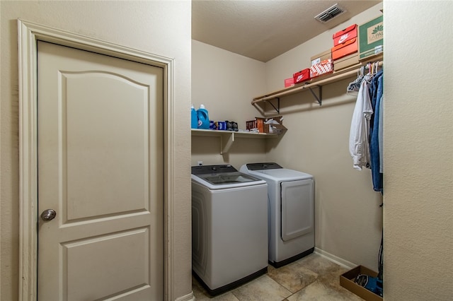 clothes washing area with a textured ceiling, washer and dryer, and light tile patterned floors