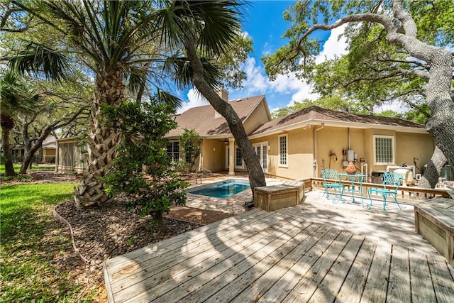 414 Olympic Dr, Rockport, TX 78382 - rear view of house featuring a wooden deck, a chimney, an outdoor pool, and stucco siding