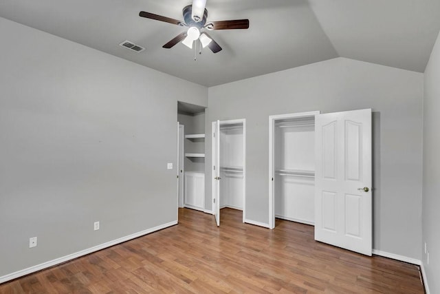 unfurnished bedroom featuring multiple closets, lofted ceiling, visible vents, light wood-style floors, and baseboards