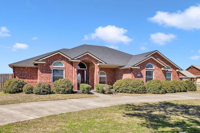 ranch-style house featuring roof with shingles, brick siding, and a front lawn