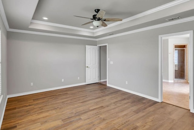 spare room featuring a raised ceiling, crown molding, light wood-style flooring, and baseboards