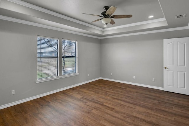 empty room with dark wood-type flooring, a ceiling fan, visible vents, baseboards, and a raised ceiling