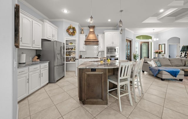 kitchen featuring an island with sink, appliances with stainless steel finishes, backsplash, white cabinets, and light stone counters