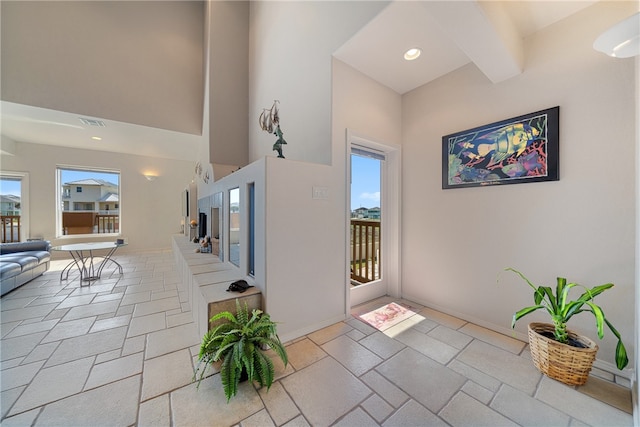 foyer entrance featuring a wealth of natural light, a towering ceiling, and beam ceiling