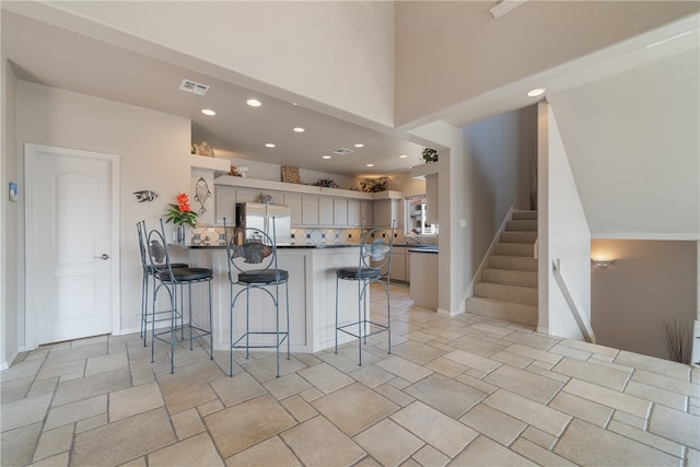 kitchen with a kitchen breakfast bar, gray cabinets, kitchen peninsula, and stainless steel refrigerator