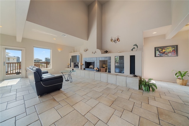 living room featuring beamed ceiling, a tiled fireplace, and a towering ceiling