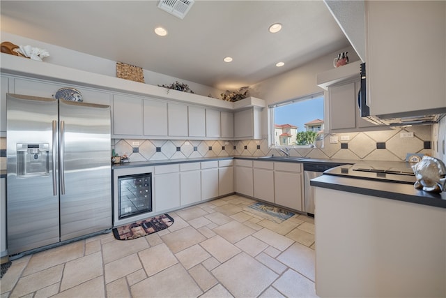 kitchen with stainless steel appliances, beverage cooler, decorative backsplash, sink, and white cabinetry