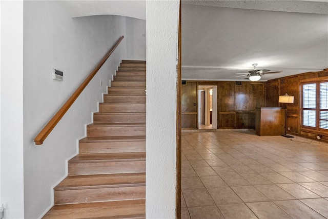 staircase featuring wood walls, tile patterned flooring, and ceiling fan