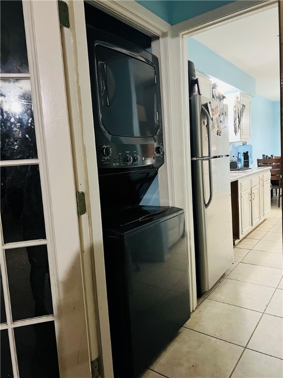 kitchen with stacked washer / dryer, fridge, white cabinetry, and light tile patterned flooring