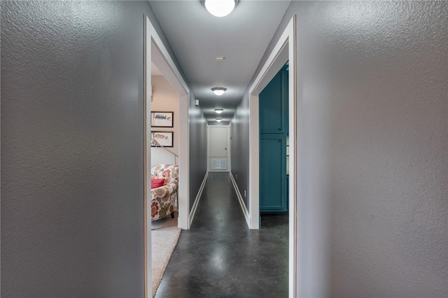 hall featuring baseboards, finished concrete floors, and a textured wall