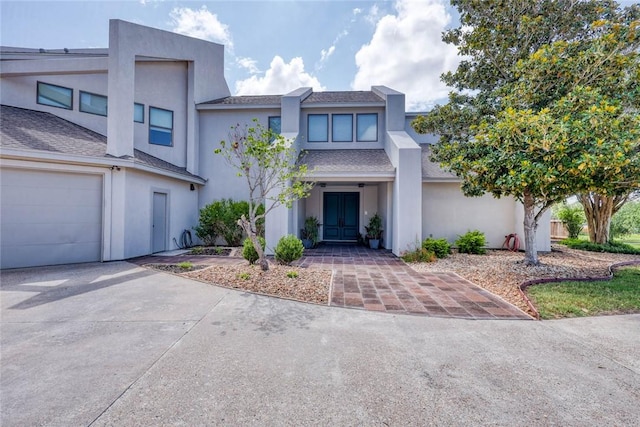 view of front of home featuring roof with shingles, stucco siding, french doors, a garage, and driveway