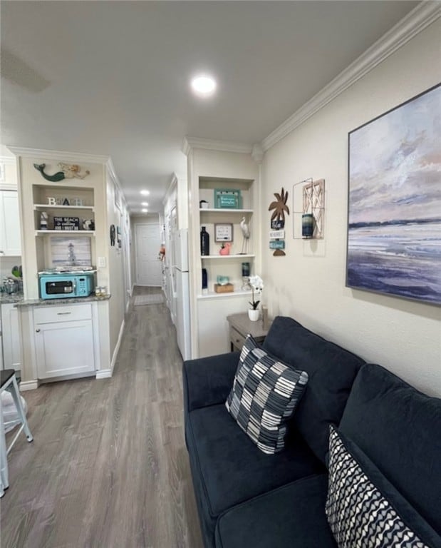 living room featuring built in shelves, light hardwood / wood-style floors, and crown molding