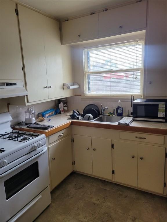 kitchen featuring sink, gas range gas stove, tile countertops, decorative backsplash, and white cabinets