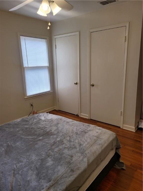 bedroom featuring multiple closets, ceiling fan, and dark hardwood / wood-style flooring