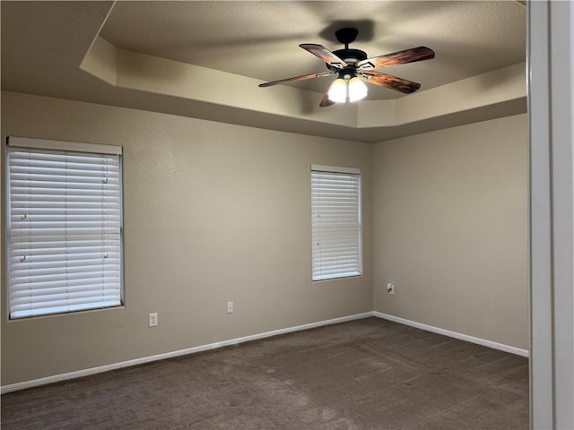 carpeted spare room with a raised ceiling and ceiling fan