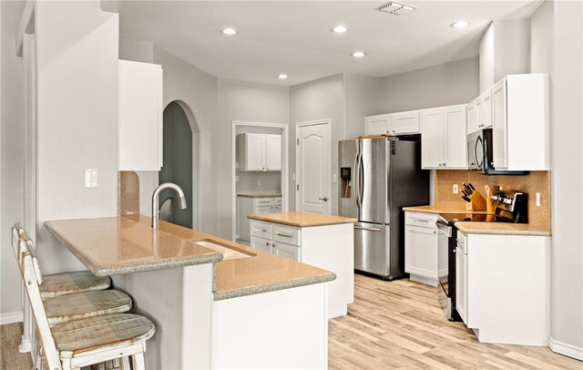 15822 Portillo Dr, Corpus Christi, TX 78418 - kitchen featuring stainless steel appliances, a peninsula, light wood-style floors, arched walkways, and white cabinets