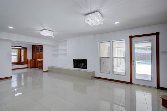 unfurnished living room featuring light tile patterned floors, a healthy amount of sunlight, a tile fireplace, and an inviting chandelier