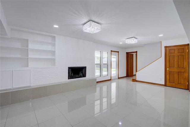 unfurnished living room with a fireplace, built in features, light tile patterned flooring, and a chandelier