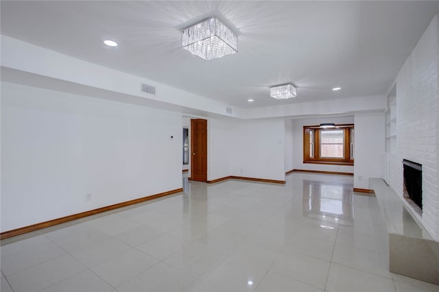 empty room with a notable chandelier, light tile patterned floors, and a brick fireplace