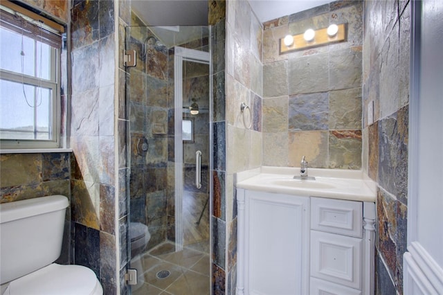 bathroom with a shower with door, vanity, toilet, and tile walls