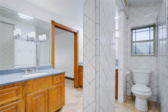 bathroom featuring toilet, vanity, tile patterned flooring, and tile walls