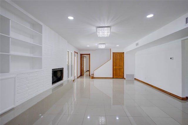 unfurnished living room with a brick fireplace, built in features, light tile patterned floors, and an inviting chandelier