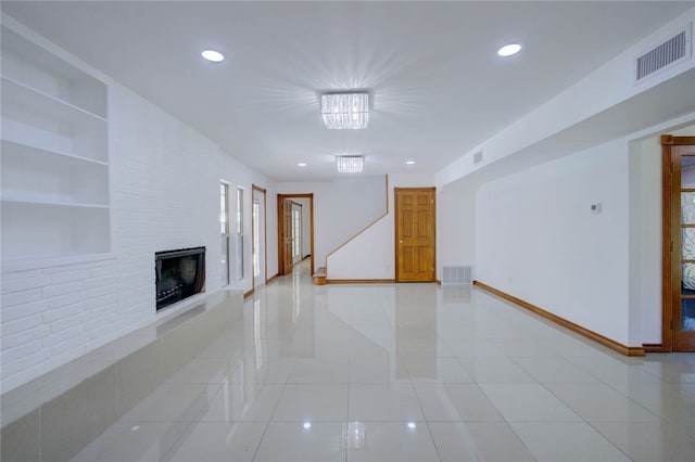 unfurnished living room with built in shelves, light tile patterned floors, a large fireplace, and a notable chandelier