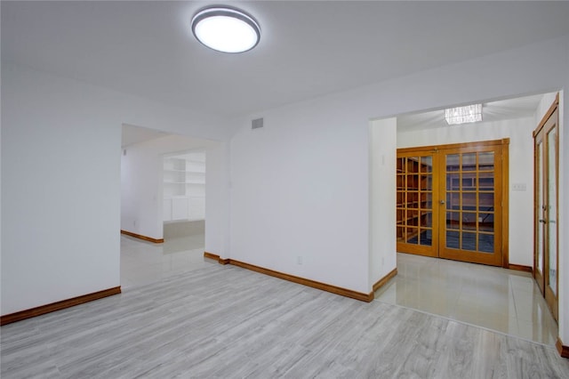 empty room featuring built in shelves, french doors, and light hardwood / wood-style floors