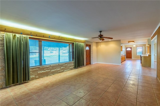 empty room with ceiling fan, a healthy amount of sunlight, light tile patterned floors, and brick wall