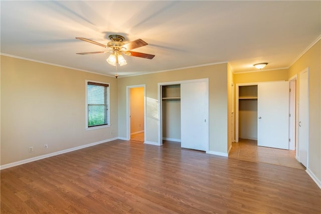 unfurnished bedroom featuring hardwood / wood-style floors, ceiling fan, crown molding, and two closets