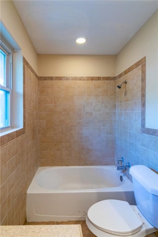 bathroom with toilet, tile walls, and tiled shower / bath