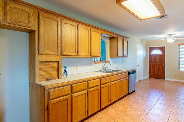 kitchen with decorative backsplash, stainless steel dishwasher, sink, light tile patterned floors, and tile counters