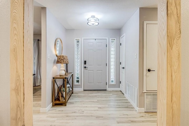 foyer entrance with baseboards, visible vents, and light wood finished floors