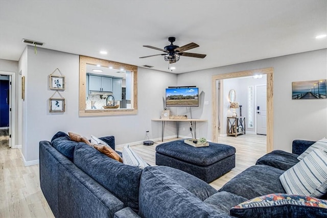 living room featuring ceiling fan, light wood finished floors, visible vents, and baseboards