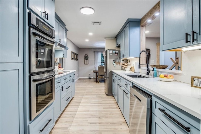 kitchen with visible vents, light wood-style flooring, appliances with stainless steel finishes, a sink, and light stone countertops