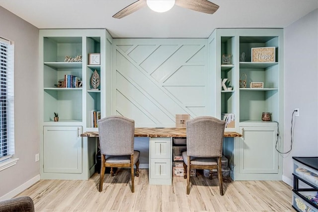 office featuring light wood finished floors, baseboards, a ceiling fan, built in shelves, and built in desk