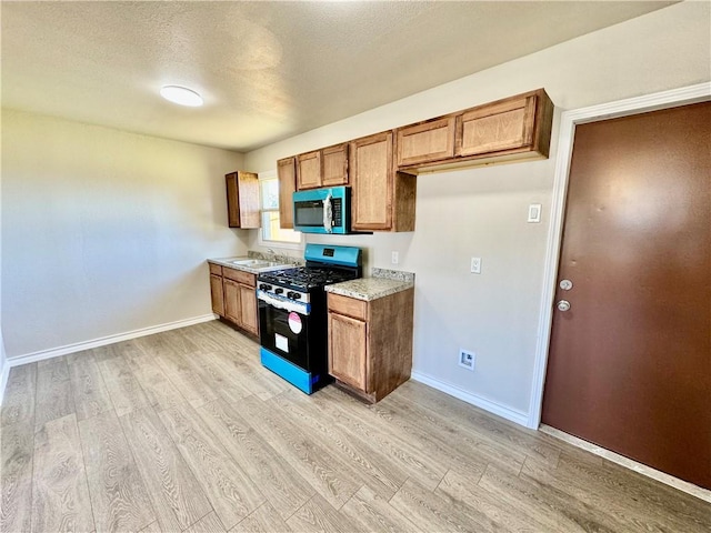 kitchen featuring black range with gas stovetop, light hardwood / wood-style flooring, a textured ceiling, and sink