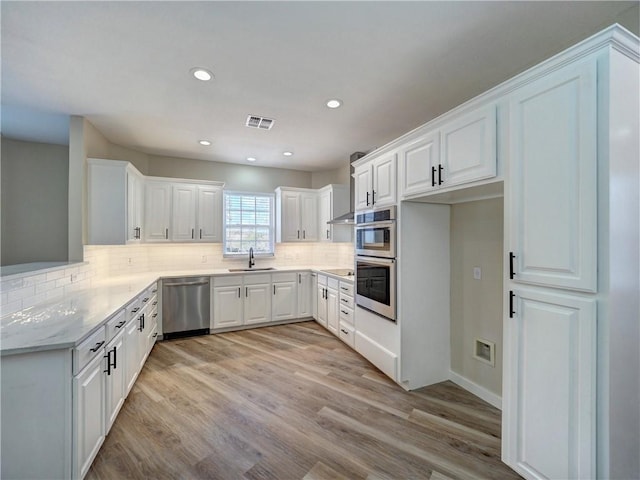 kitchen featuring white cabinetry, sink, decorative backsplash, appliances with stainless steel finishes, and light wood-type flooring