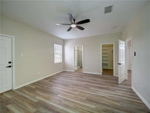 unfurnished bedroom with ensuite bathroom, ceiling fan, a spacious closet, light hardwood / wood-style flooring, and a closet