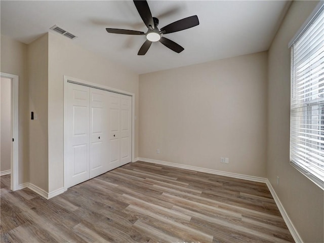 unfurnished bedroom featuring multiple windows, light wood-type flooring, a closet, and ceiling fan