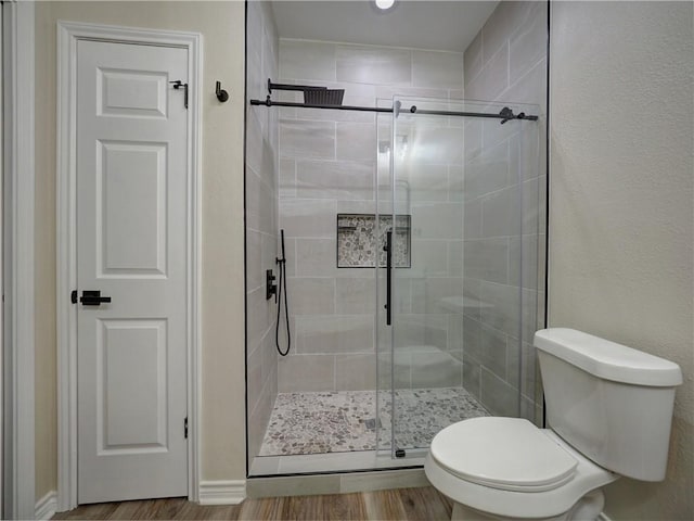 bathroom with toilet, a shower with shower door, and wood-type flooring