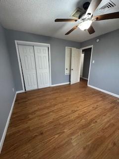 unfurnished bedroom with a textured ceiling, wood finished floors, a ceiling fan, visible vents, and baseboards