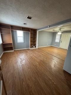 unfurnished living room with a textured ceiling, wood finished floors, built in features, and baseboards